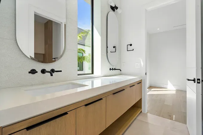 Modern bathroom with light wood vanity, white countertops, and black fixtures.