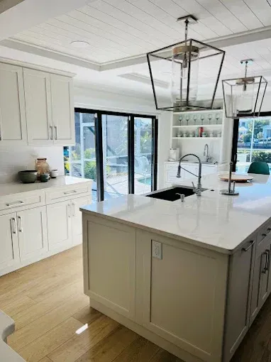 White kitchen with island, cabinets, and folding doors to a pool. Modern pendant lights.