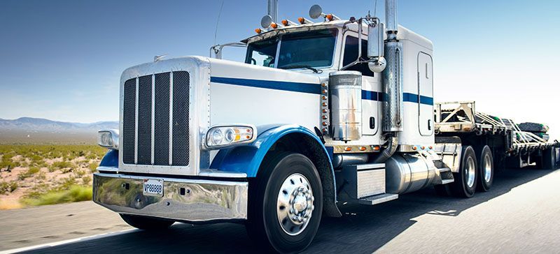 A white and blue semi truck is driving down a highway.