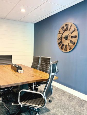 A conference room with a wooden table and chairs and a large clock on the wall.