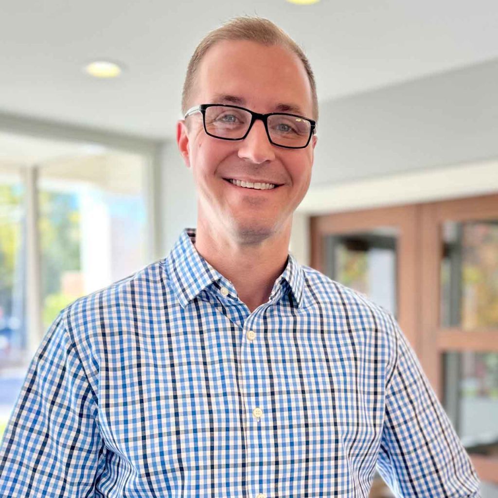 A man wearing glasses and a plaid shirt is smiling for the camera.