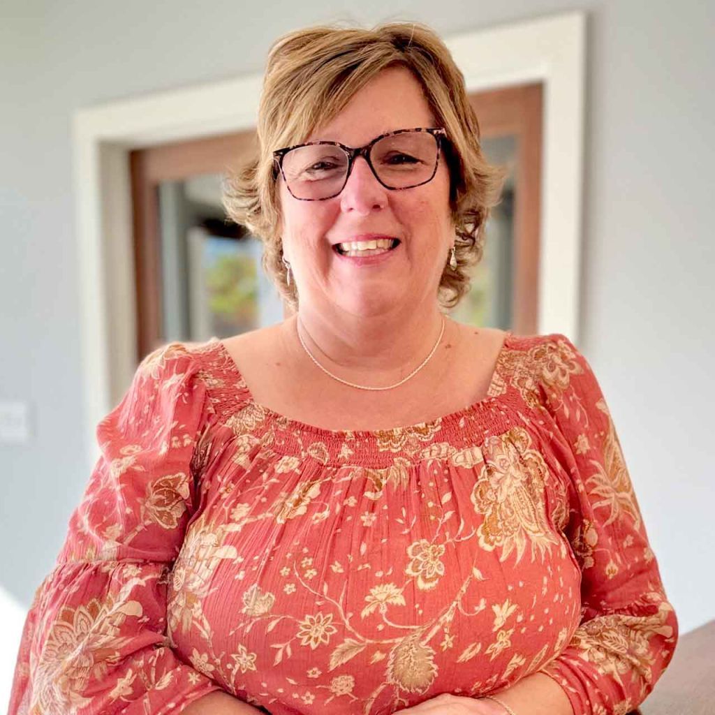 A woman wearing glasses and a red top is smiling for the camera.