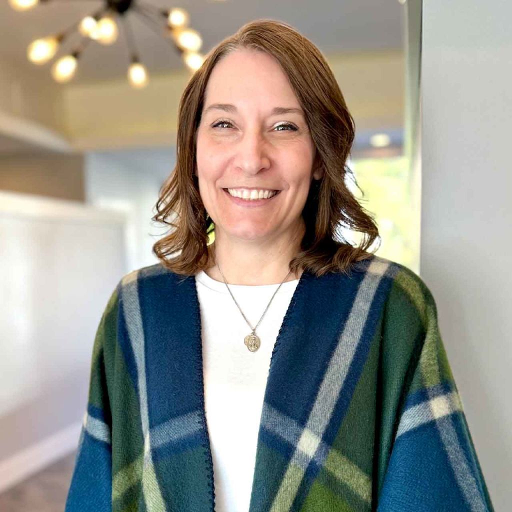 A woman wearing a plaid sweater and a necklace is smiling for the camera.