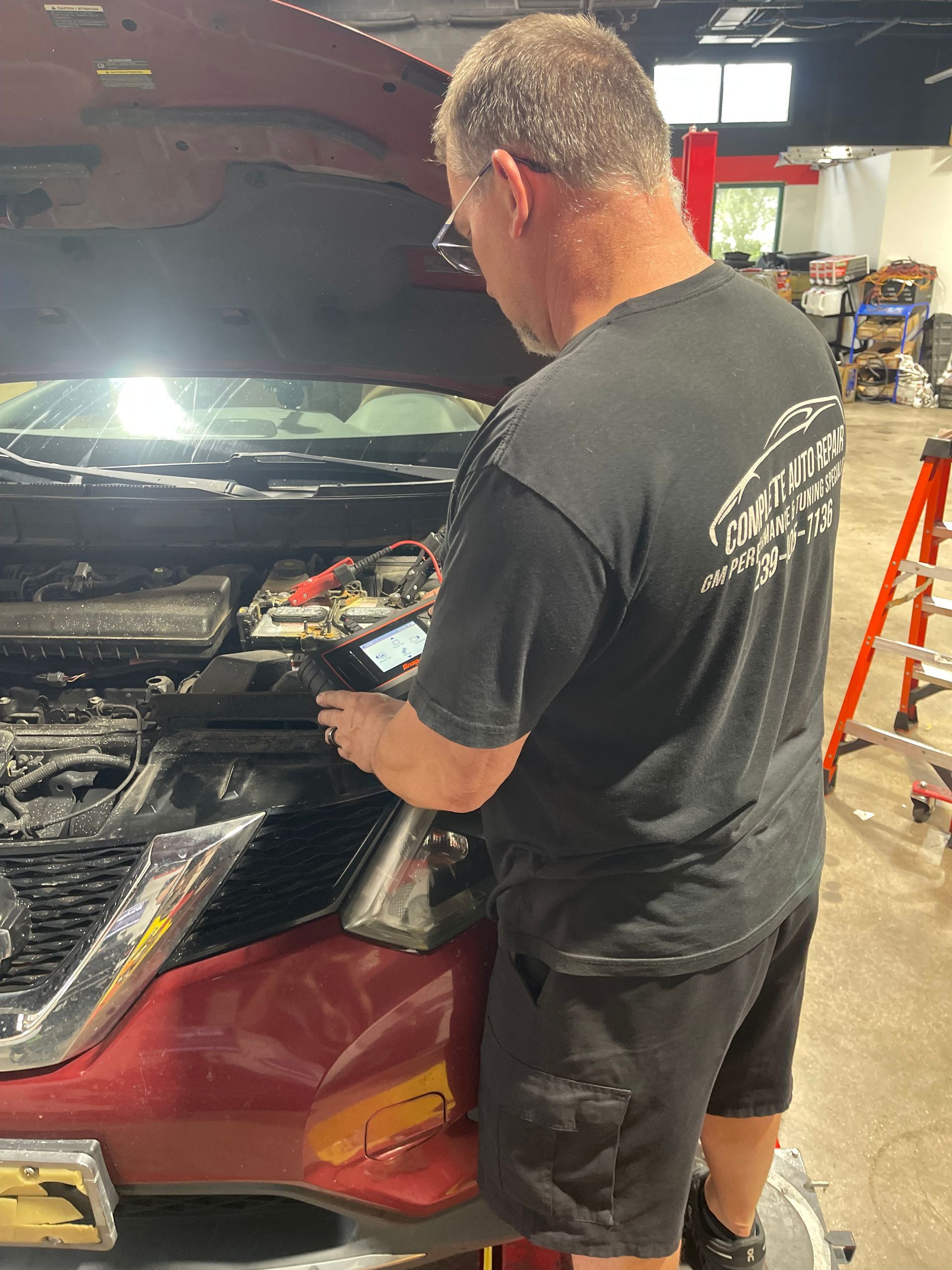 Mechanic working on a red car with the hood open in a garage.