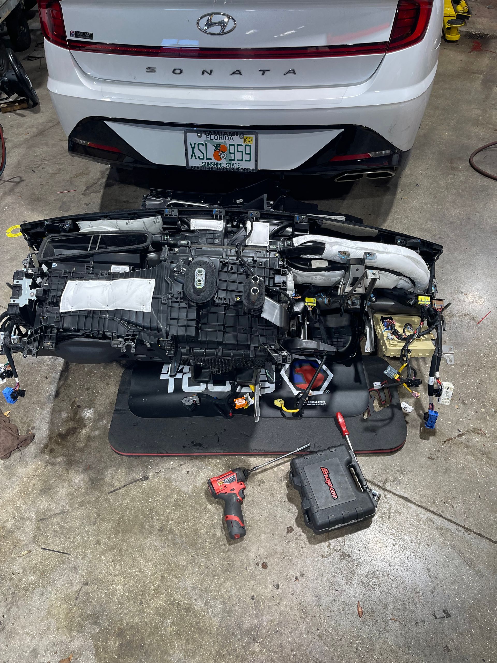 Car engine assembly on floor in front of a white Hyundai sedan, with tools nearby.