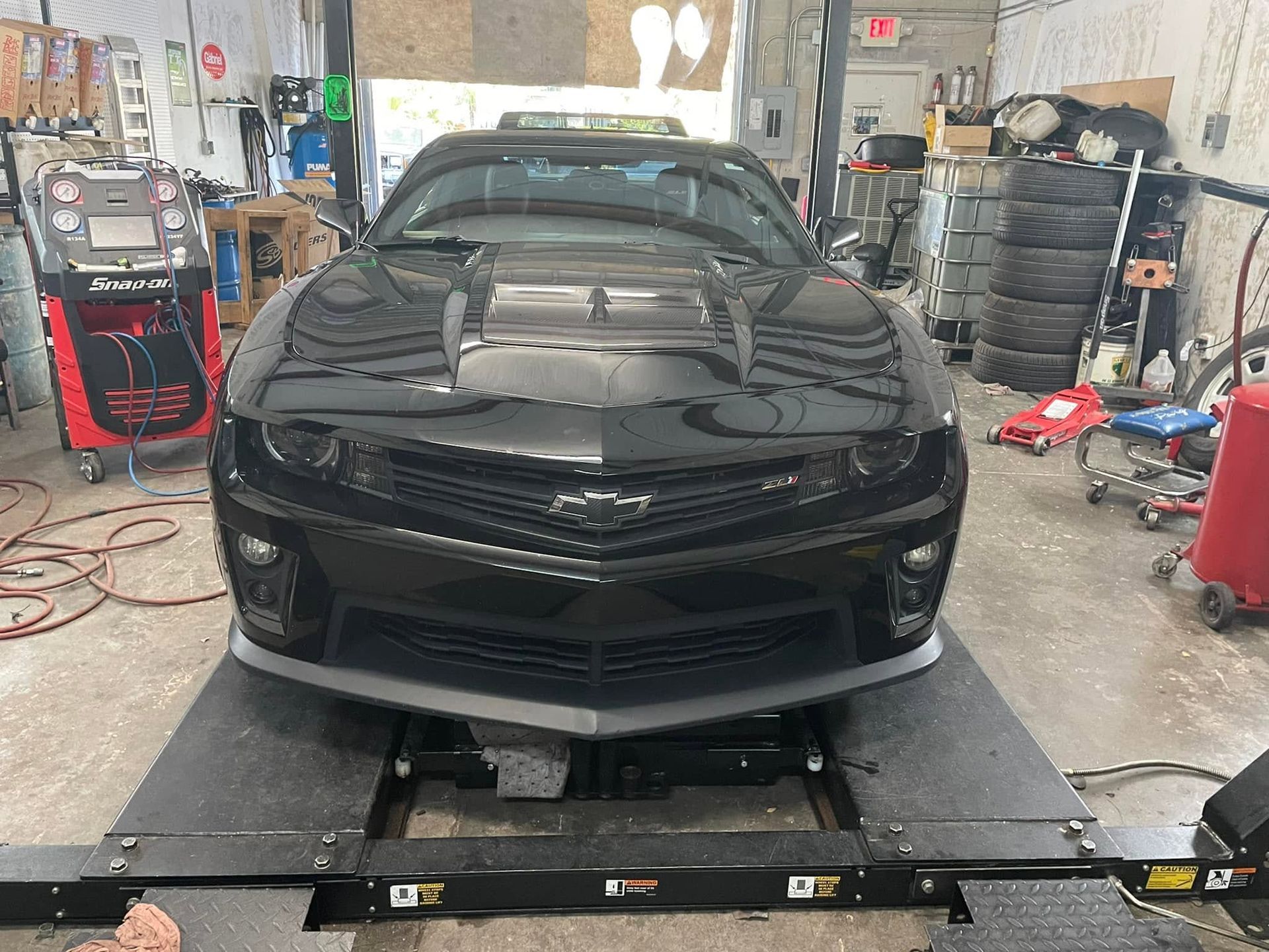 Black sports car on a lift inside an auto shop, with its hood open and tools around it.
