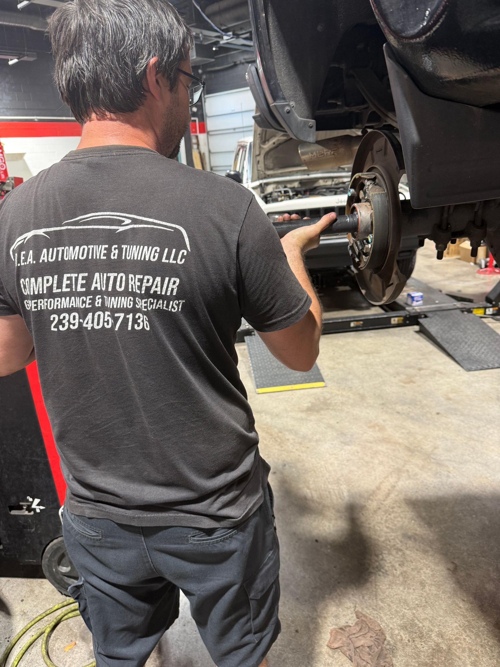 Mechanic working on a car wheel in an auto shop, viewed from behind.