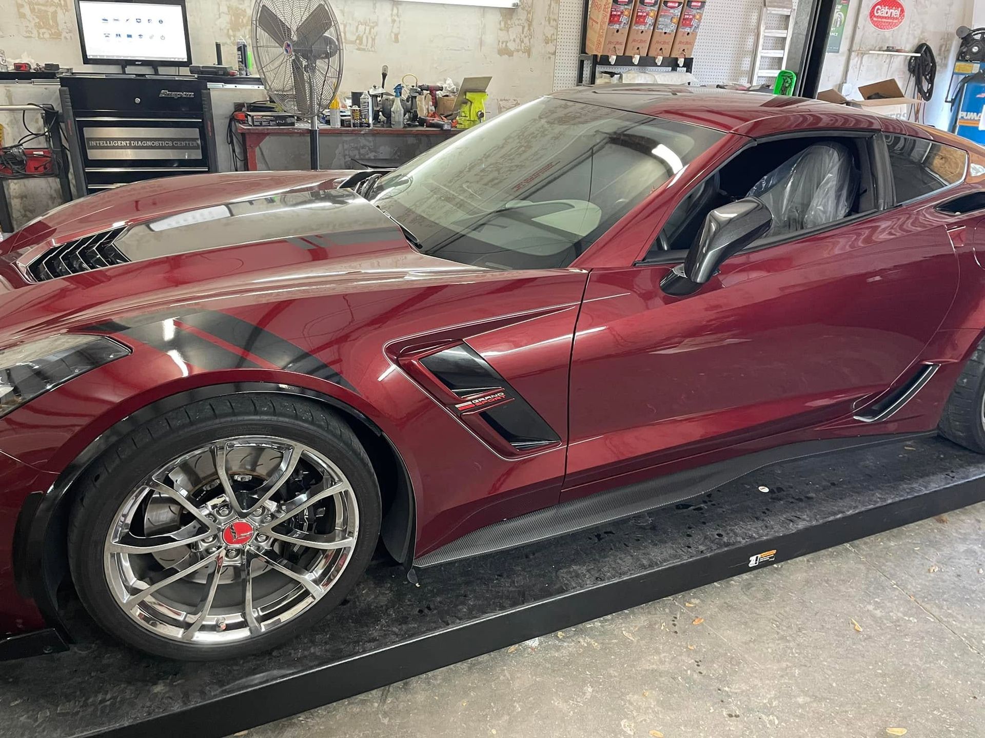 Maroon sports car on a garage lift, side view with workshop equipment in the background