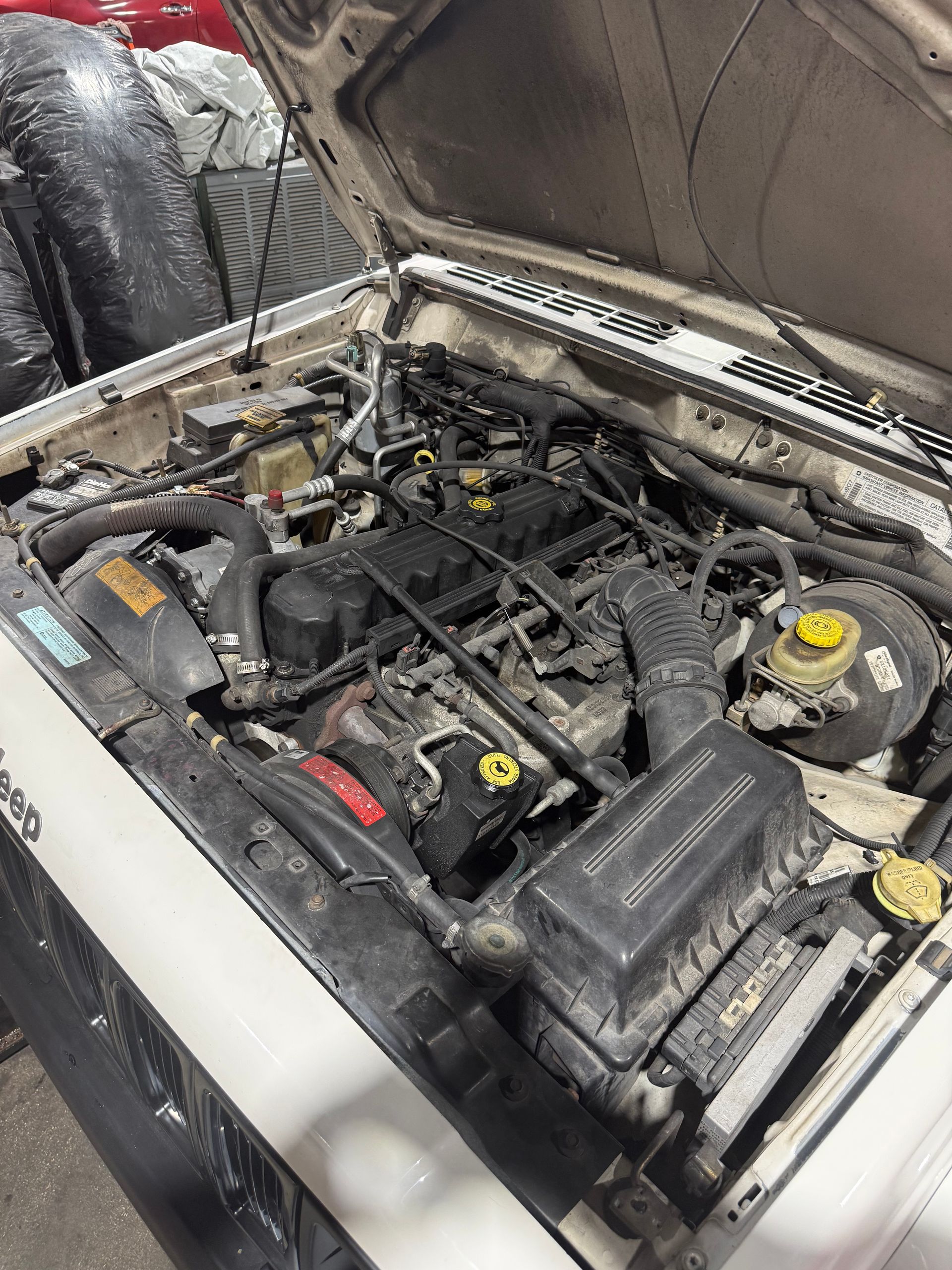 Open car hood showing an engine bay with dusty components and a yellow fluid cap.