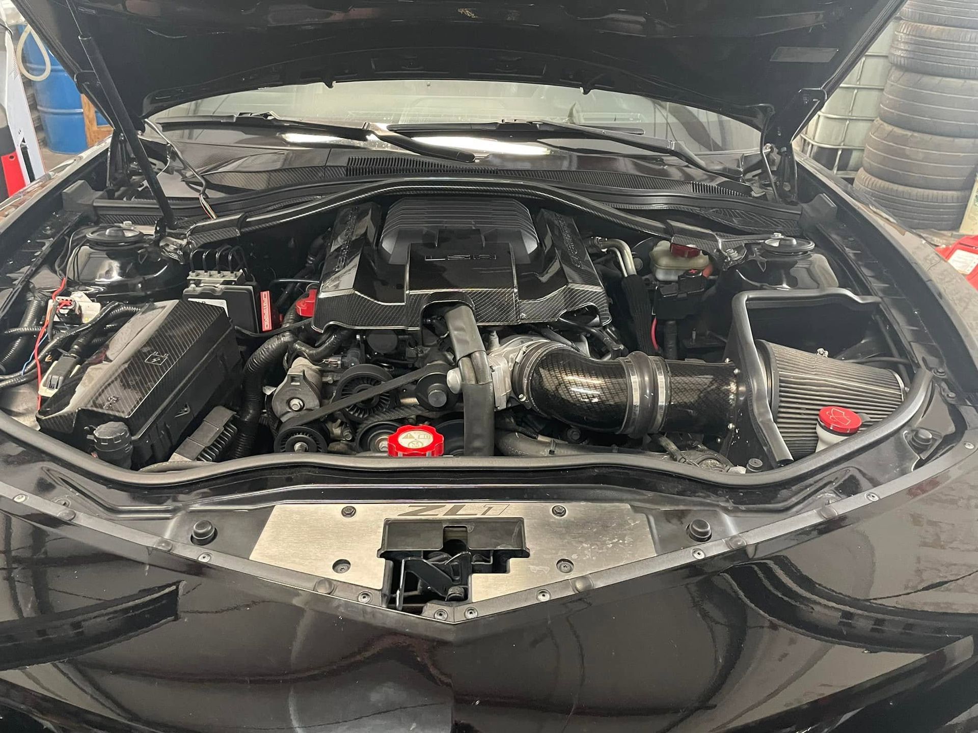 Car engine bay with hood open, showing exposed engine components and hoses.