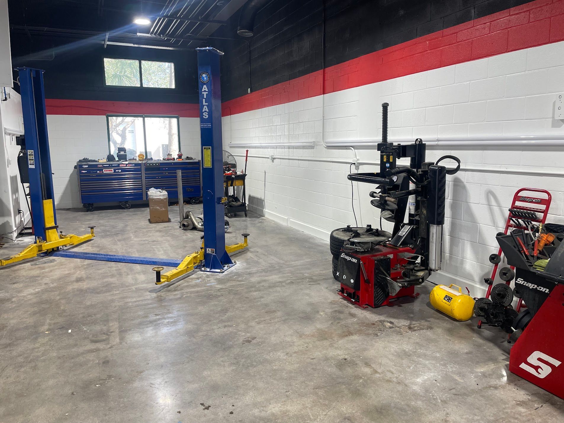 Auto repair shop with blue car lift, tools, and equipment against a white-and-red wall.