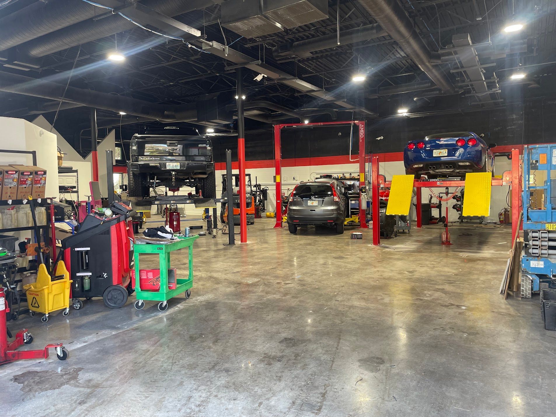 Auto repair shop interior with cars on lifts, tools, and red equipment shelves.