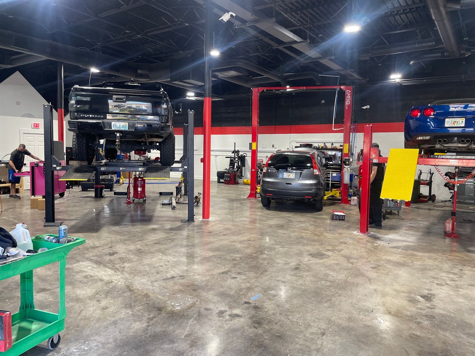Auto repair shop with cars on lifts and a black SUV centered under red support beams.