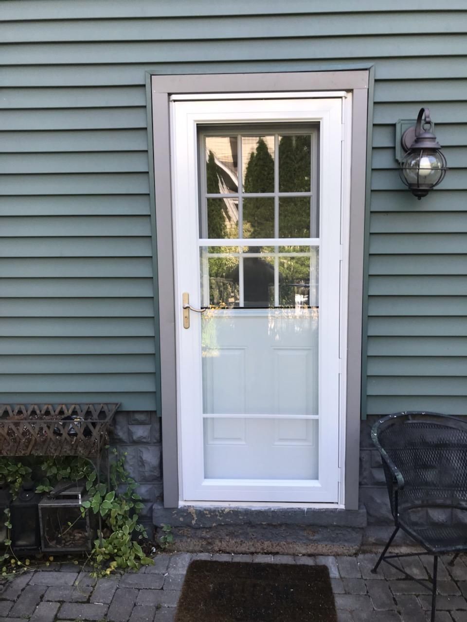 A white door is on the side of a house next to a chair.