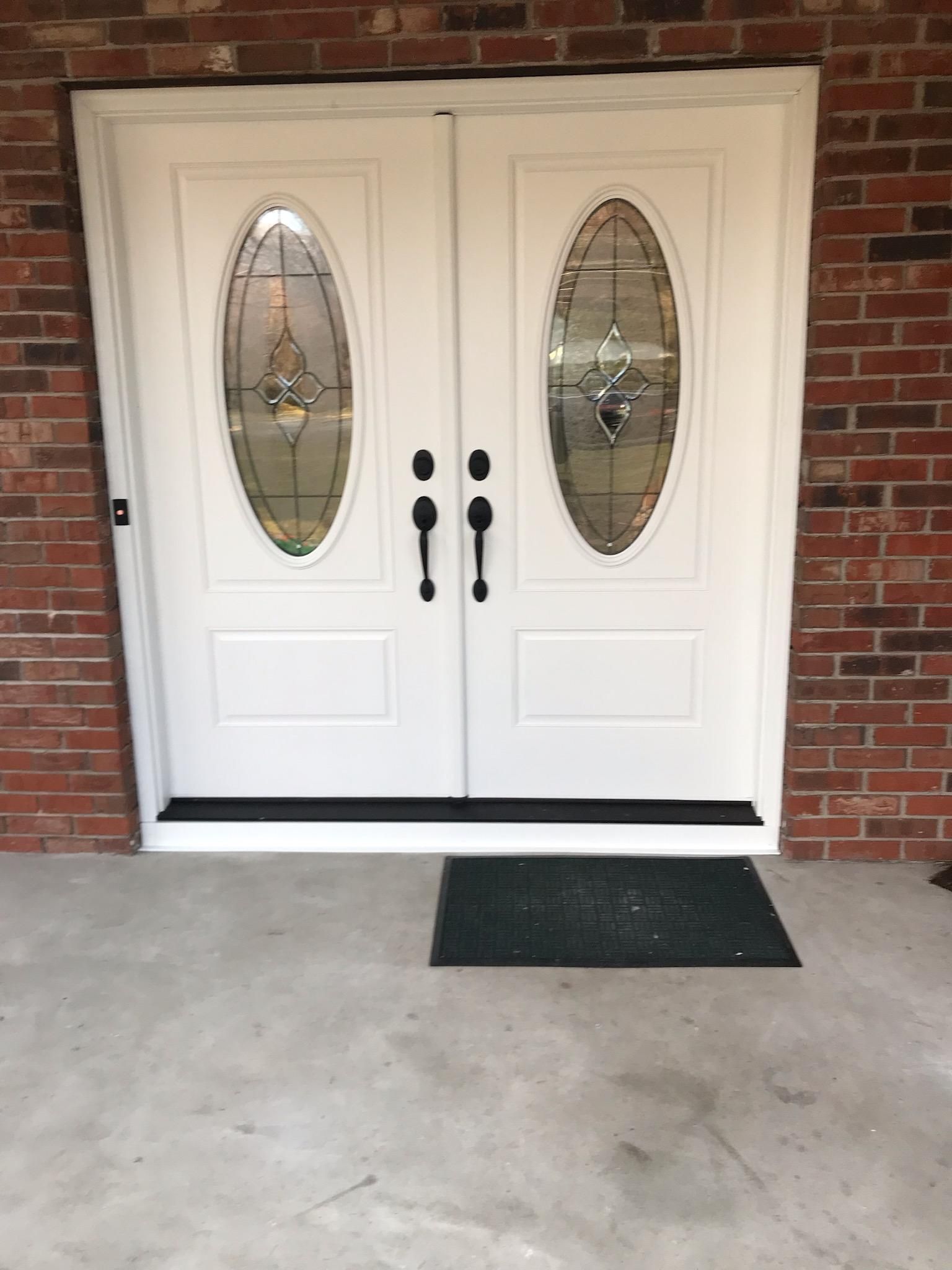 A pair of white doors with stained glass windows on a brick wall.