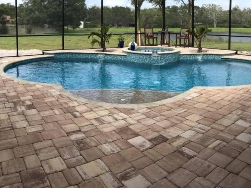 Round backyard pool with blue water, brick patio, and screened enclosure overlooking a grassy yard