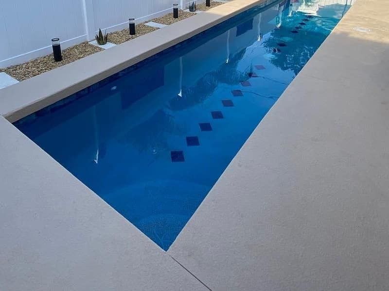 Rectangular outdoor swimming pool with clear blue water and a beige deck