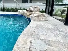 Curved backyard pool edge with stone deck and waterfall feature