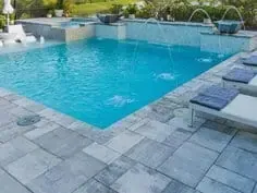 A modern outdoor swimming pool with blue water, stone deck, and lounge chairs around the edge