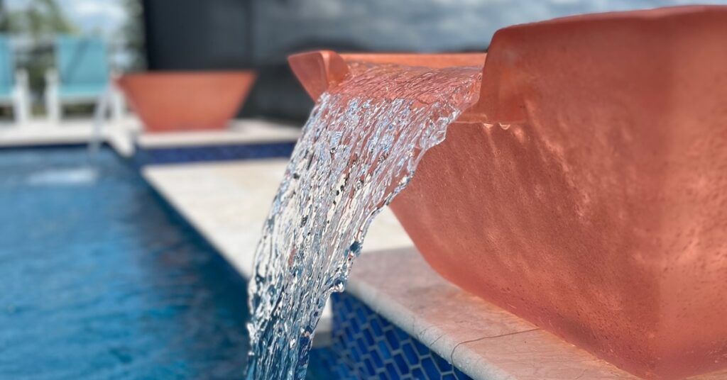 Water spilling from a terracotta pool fountain into blue tiled water.