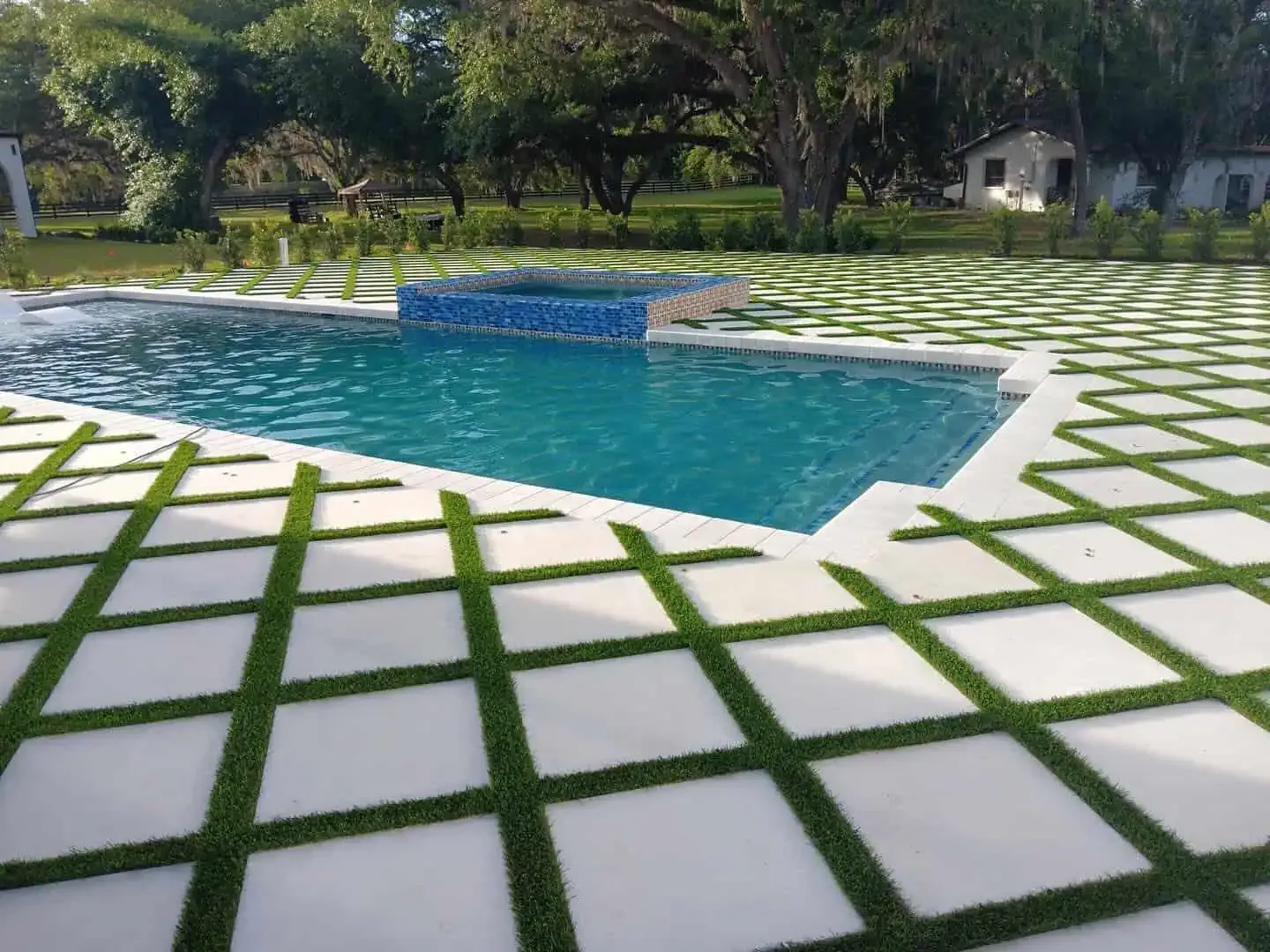 Backyard pool with blue water and white stone pavers separated by green grass lines