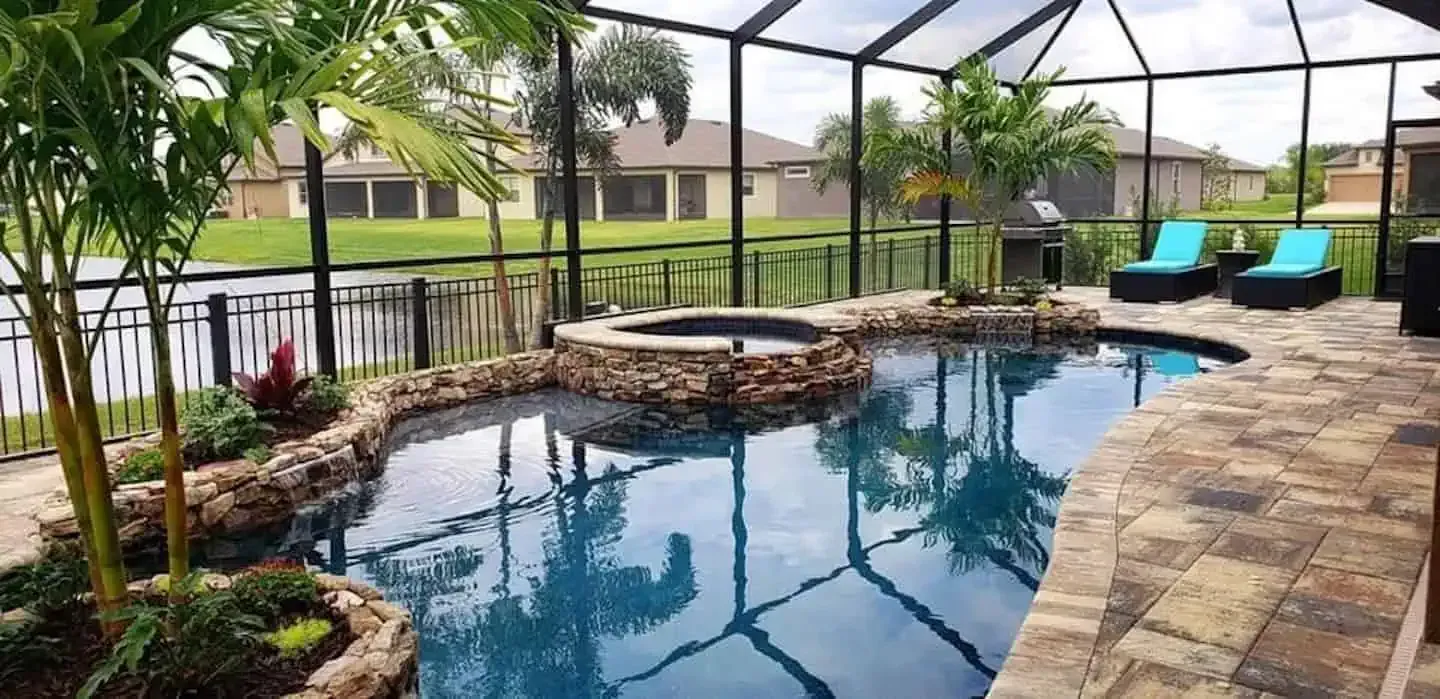 Screened backyard pool with stone deck, waterfall ledge, and blue lounge chairs overlooking a lake.