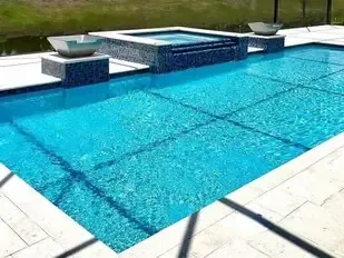 Blue swimming pool with a raised spa and white stone deck in bright sunlight
