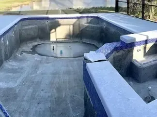 Empty concrete pool under construction with a central drain and blue-tiled edging
