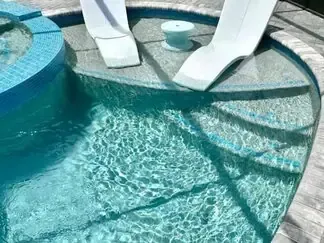Pool with turquoise water, white lounge chairs, and curved stone steps casting shadows