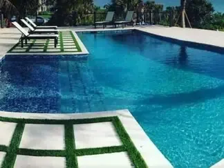 Swimming pool with turquoise water, white lounge chairs, and green-trimmed steps in the foreground