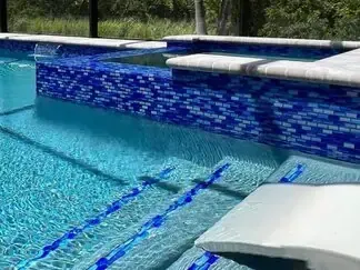 Swimming pool with blue mosaic tile wall and lane markings, plus a white diving board in the foreground