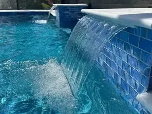 Blue swimming pool with a waterfall spillover into the water