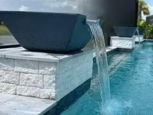 Modern black fountain spilling water into a turquoise pool beside a white stone ledge