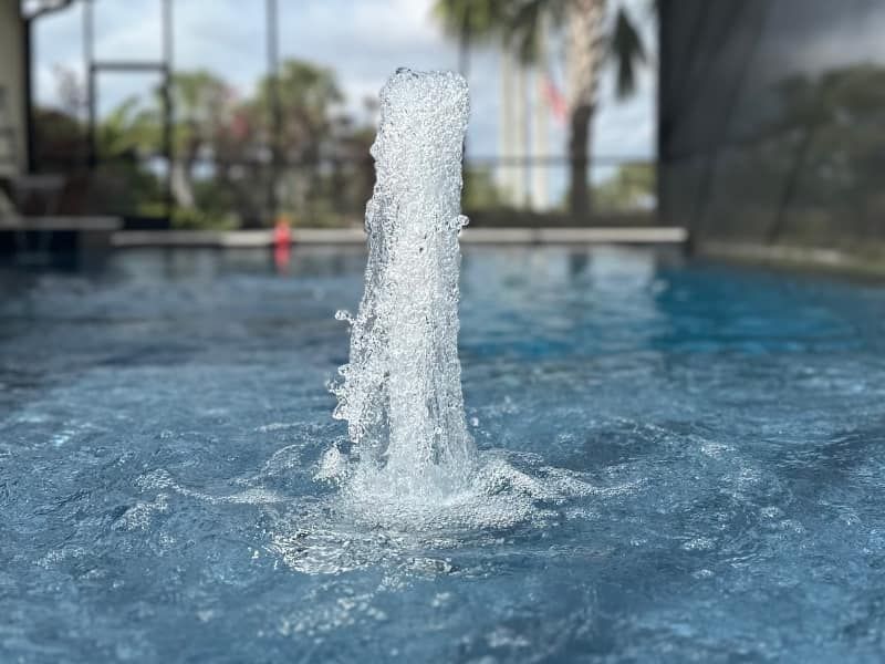 Water fountain jet splashing in a shallow pool with blurred outdoor background