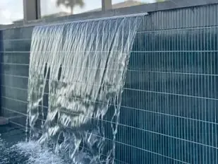Water cascading over a blue tiled wall, forming a small waterfall.