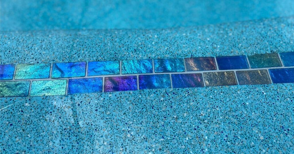 Blue pool edge with a row of iridescent mosaic tiles beneath the waterline