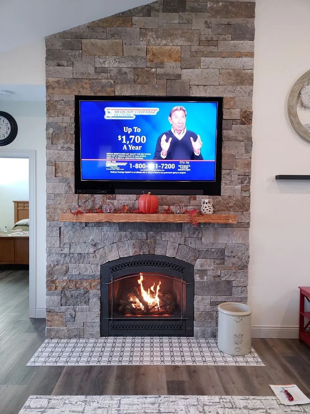Fireplace with TV mounted on a stone wall; a person is on the TV screen.