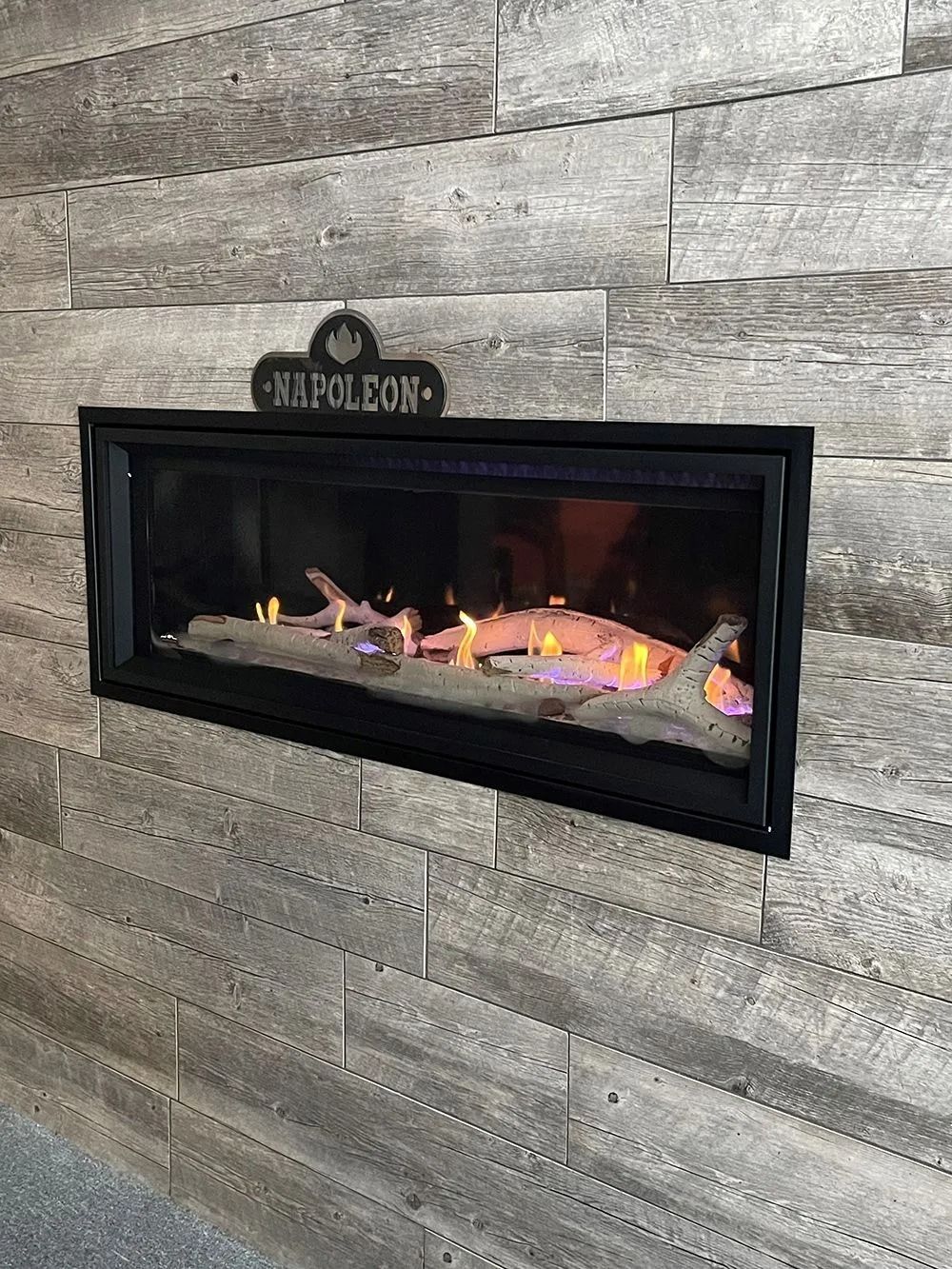 Black framed Napoleon electric fireplace inset in a gray wood-look plank wall.