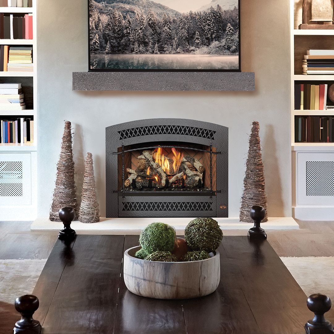 Fireplace with a lit fire, flanked by bookshelves and decorative trees. A table in front has moss balls.