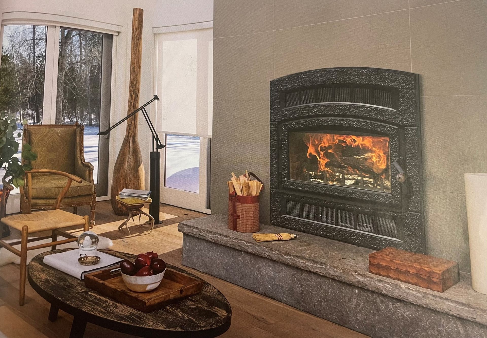 Cozy living room with fireplace, snow outside the window. Wooden furniture and decor; warm fire burning.