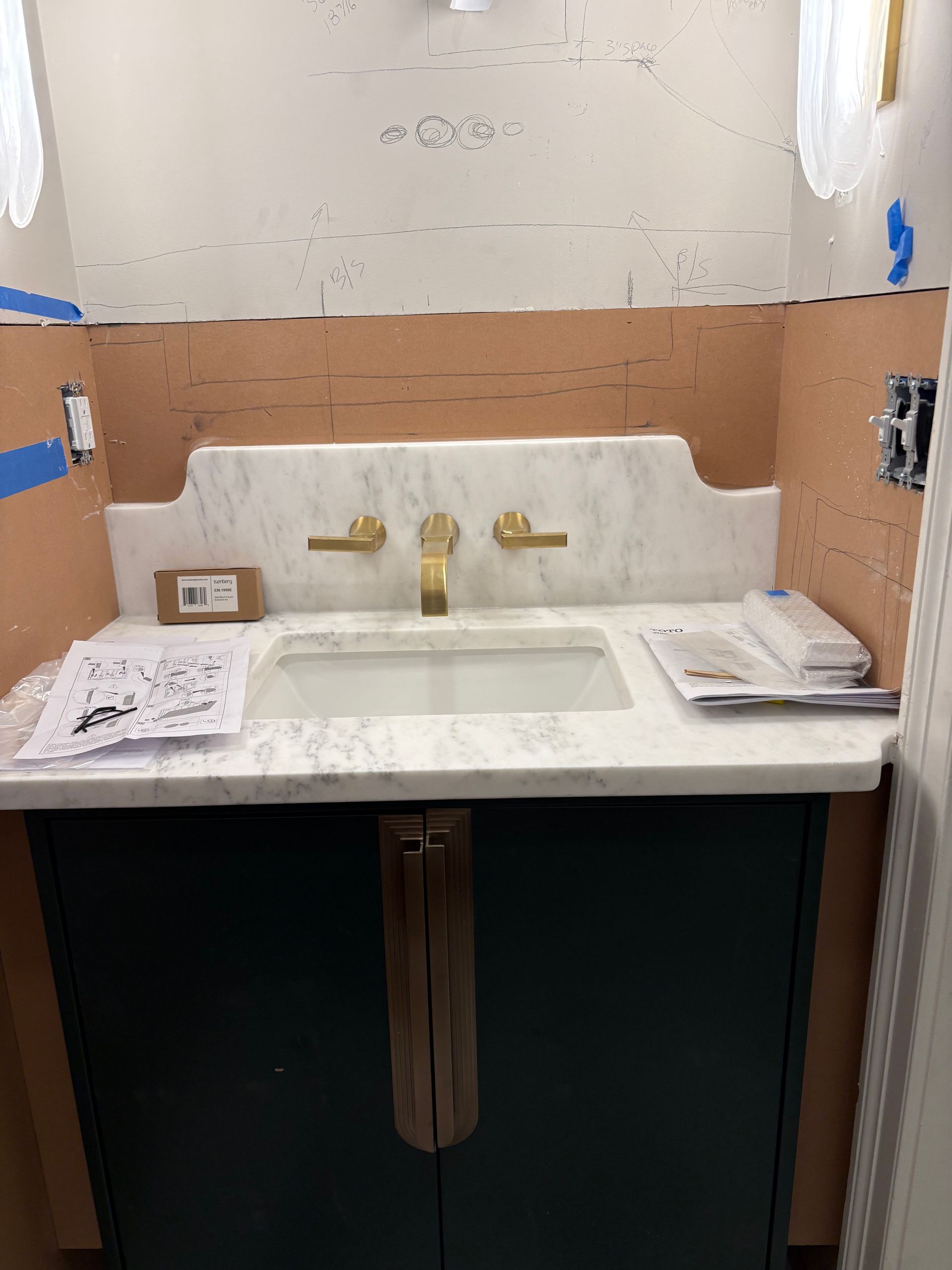 Dark green vanity with gold fixtures, white marble sink, and pinkish backsplash.