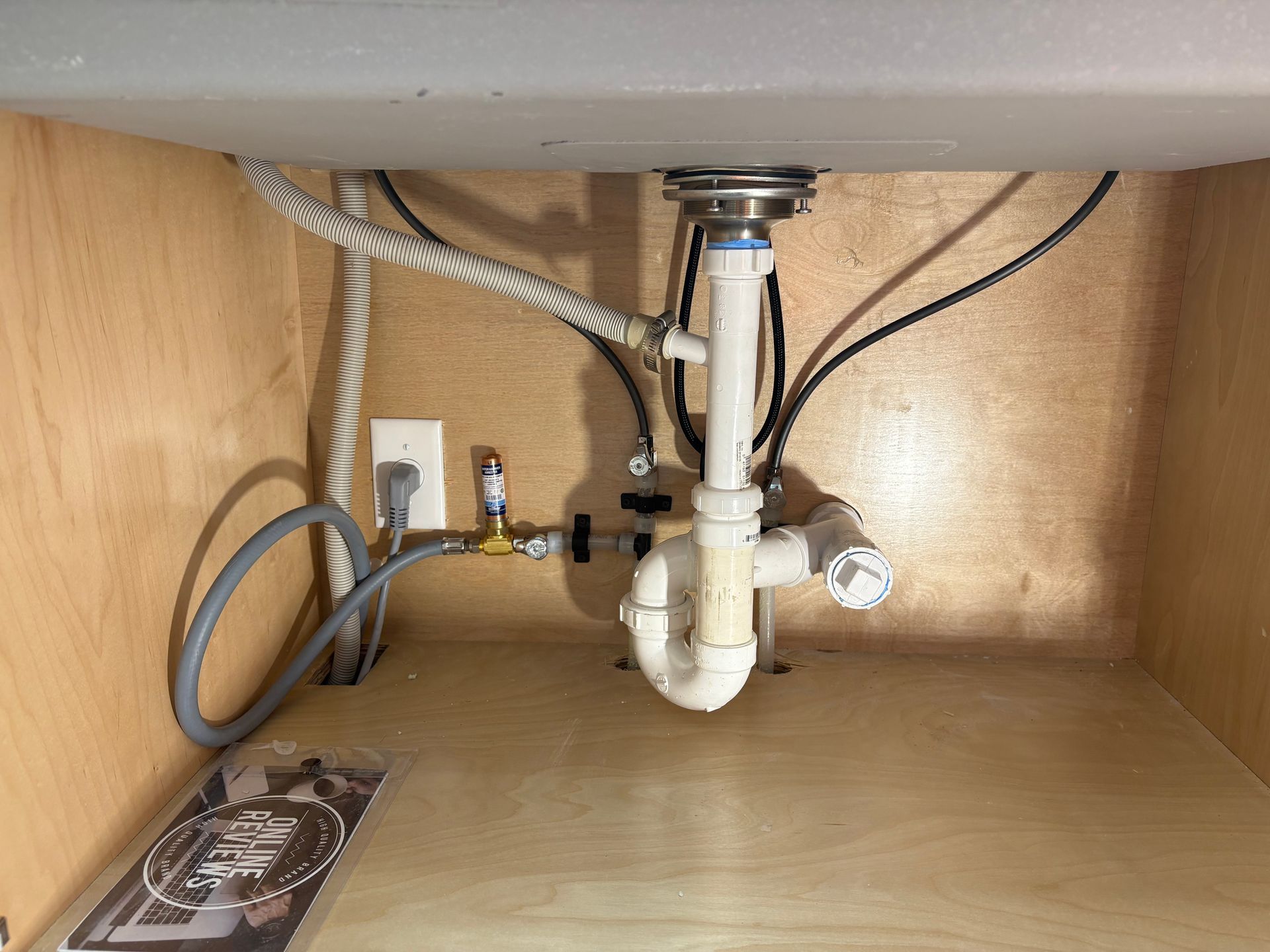 Under a sink, plumbing pipes and water lines are visible. An electrical outlet and cord are also present.