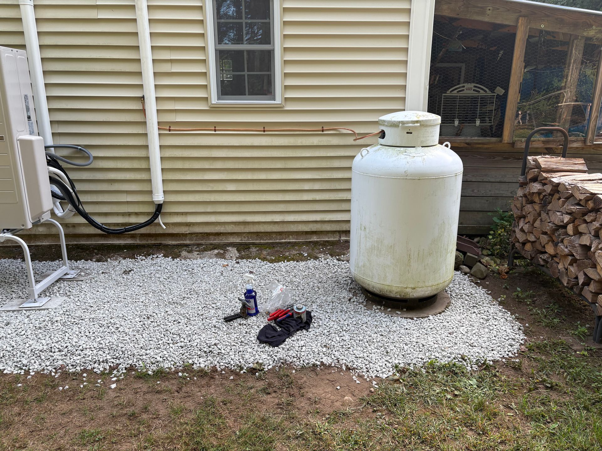 Propane tank beside a beige building on a bed of white gravel, with shoes and tools on the ground.