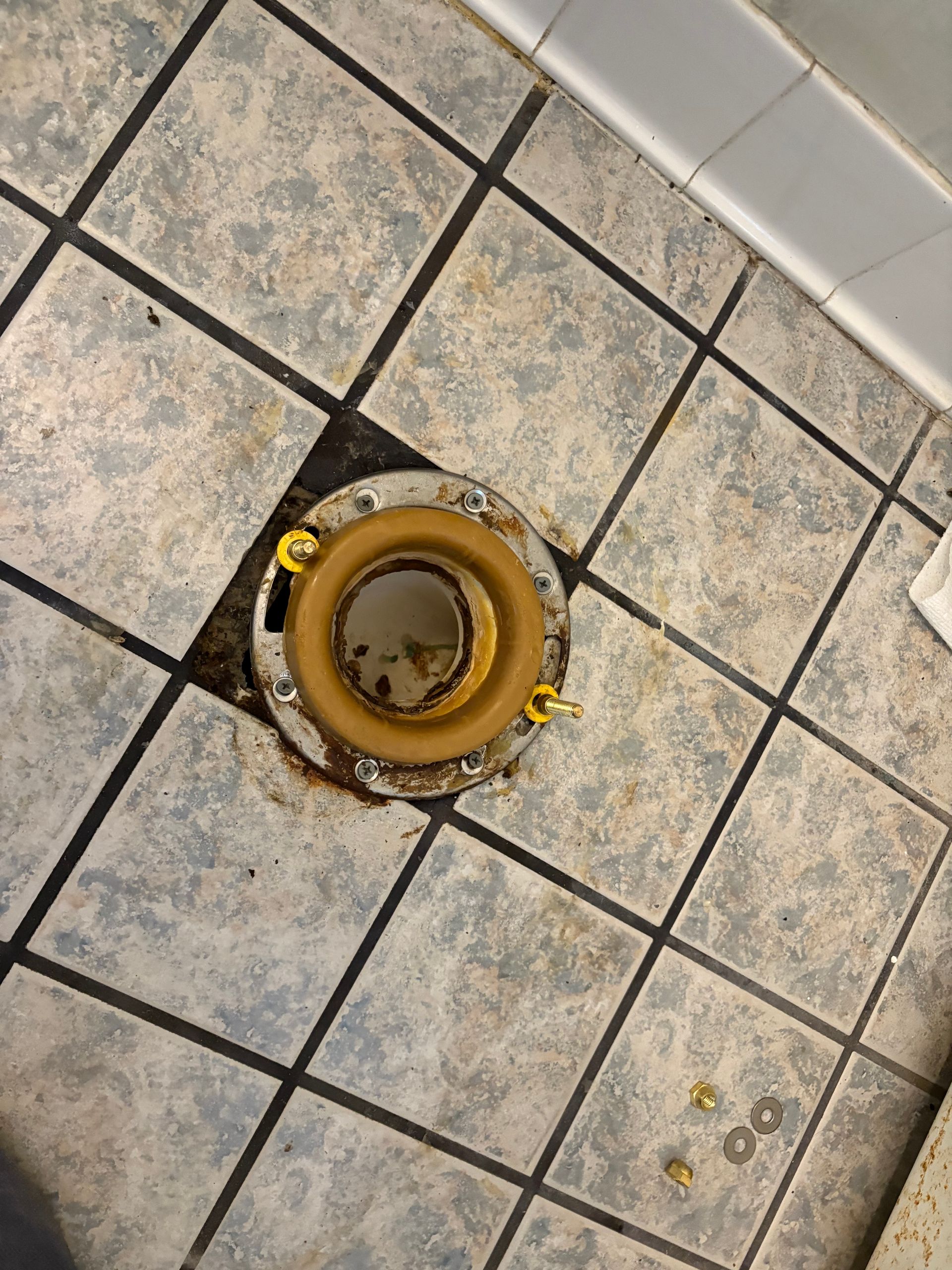 Toilet flange on bathroom tile floor, showing a wax ring.  Small screws and washers on the tiles.