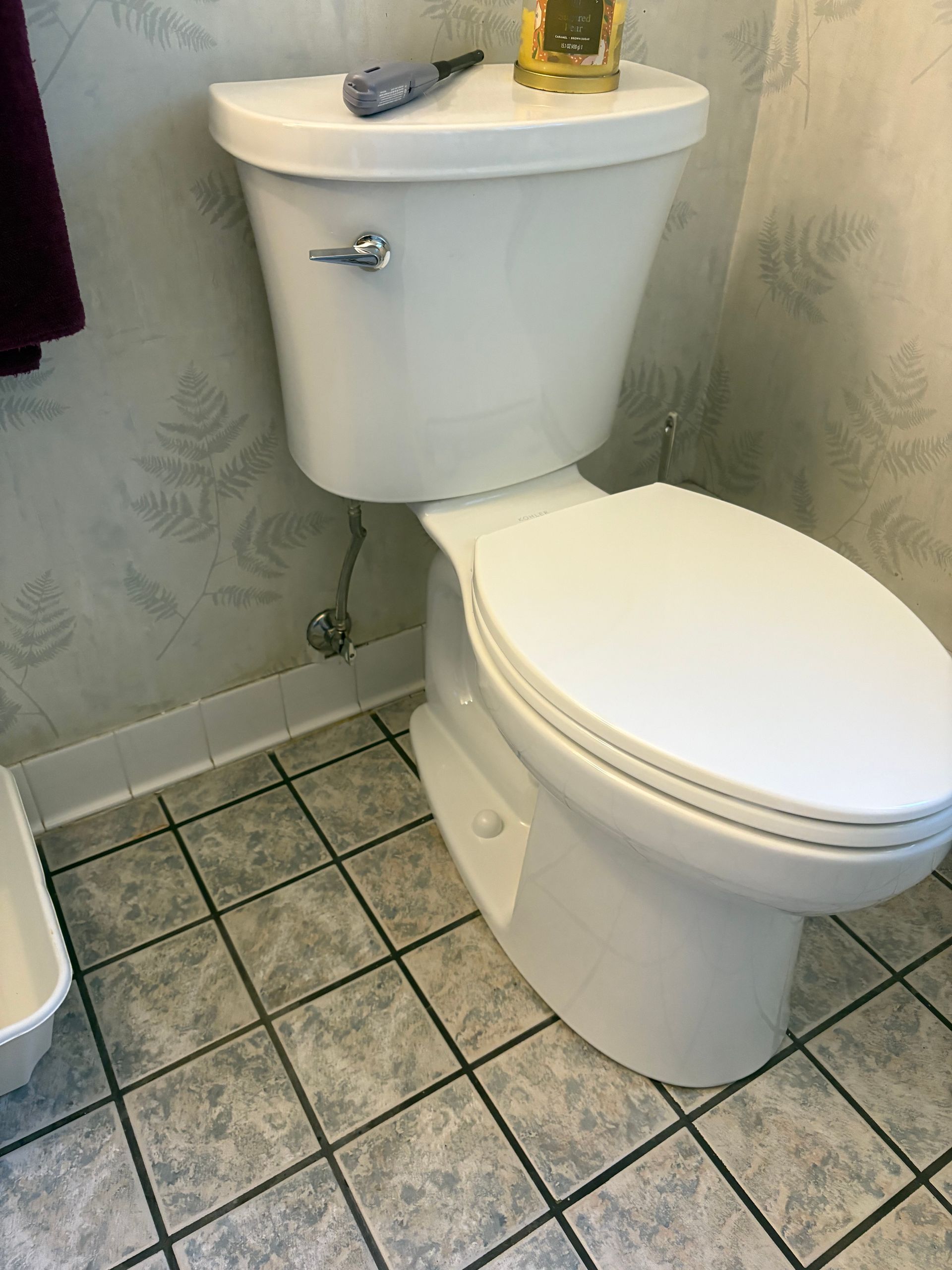 White toilet in a bathroom with floral wallpaper and tile flooring.