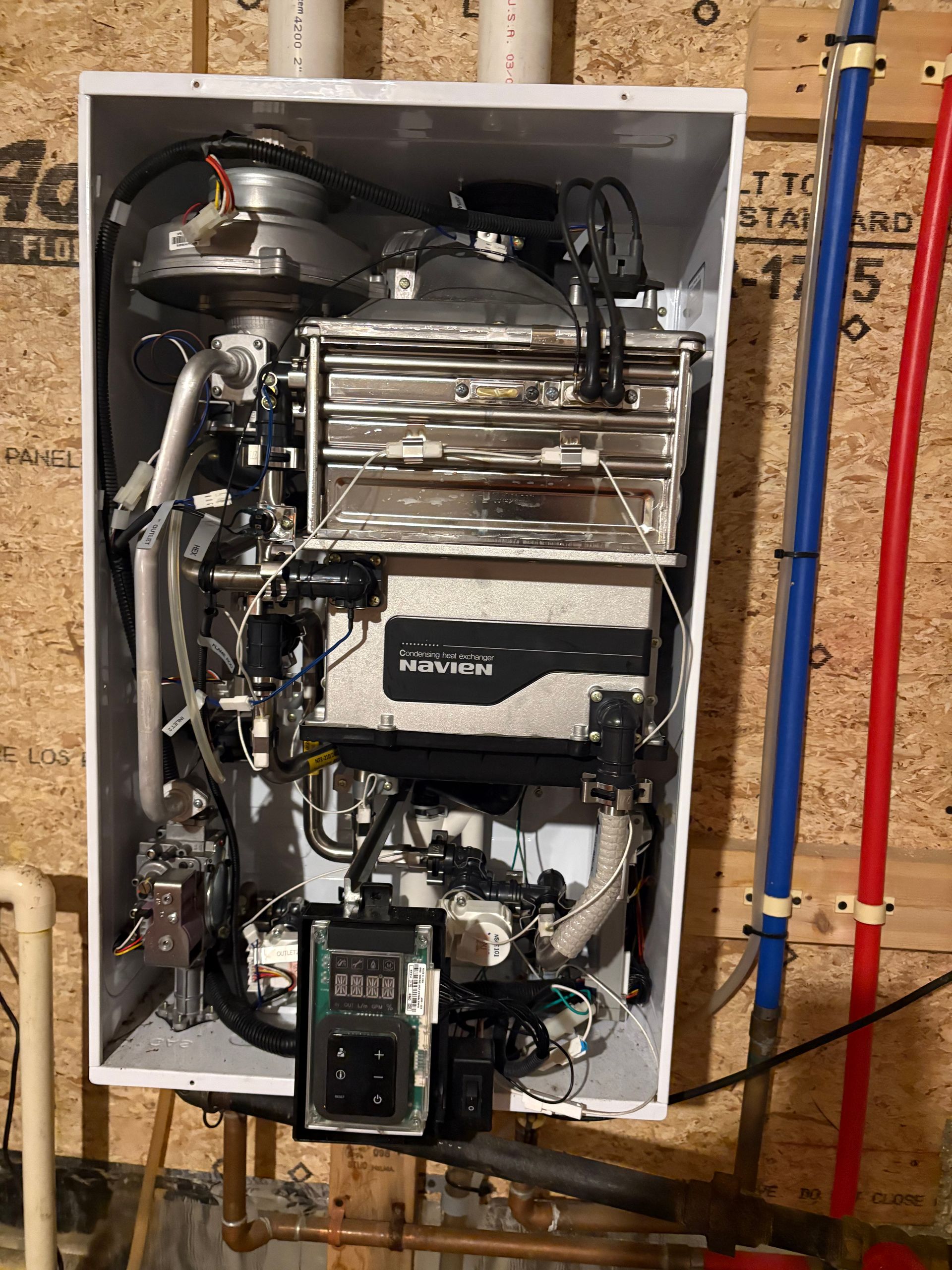 Wall-mounted condensing boiler unit with visible internal components. Blue/red pipes on right, white flue pipes on top.
