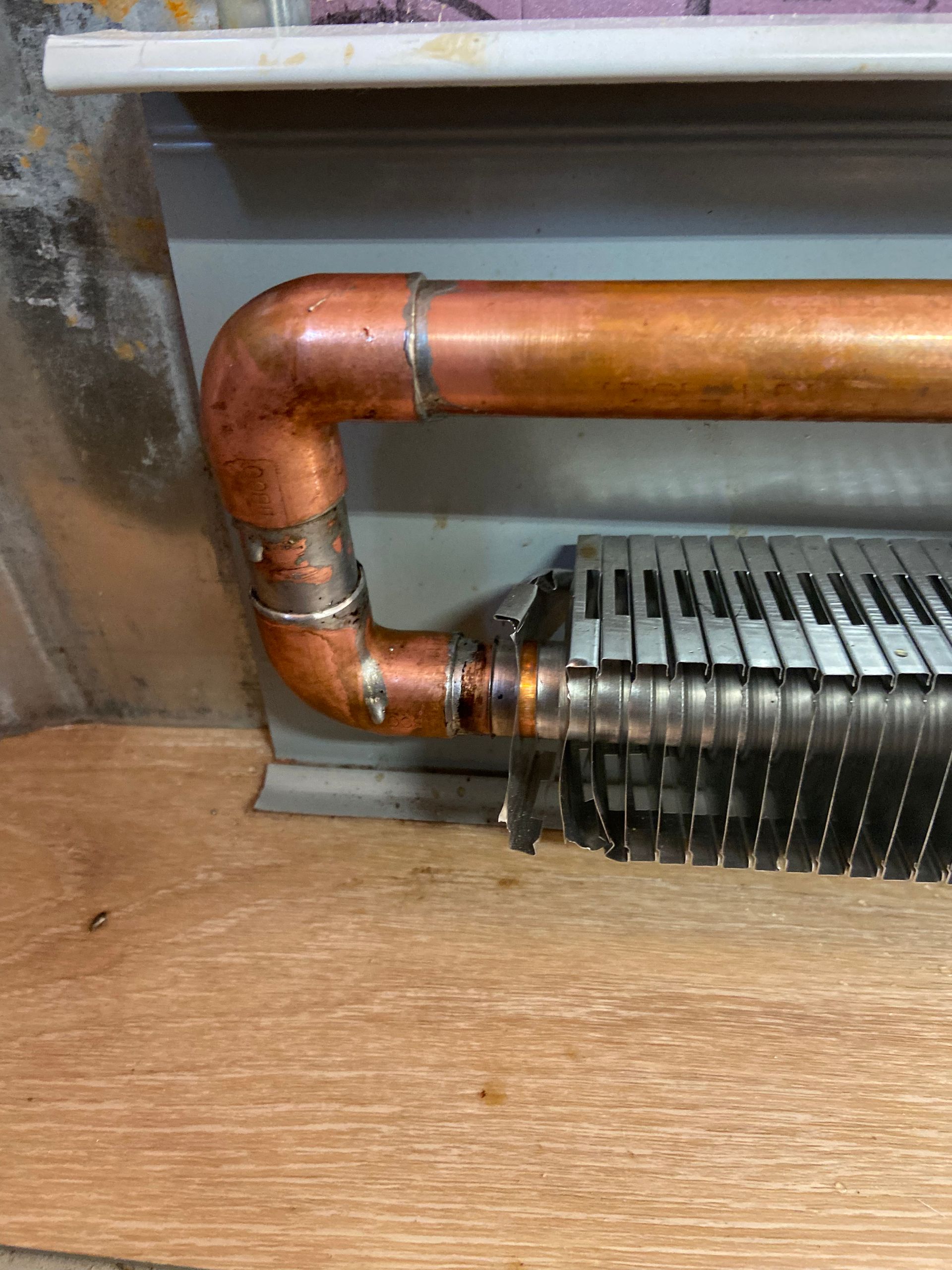 Copper pipe connected to a finned heater, near a wooden surface.