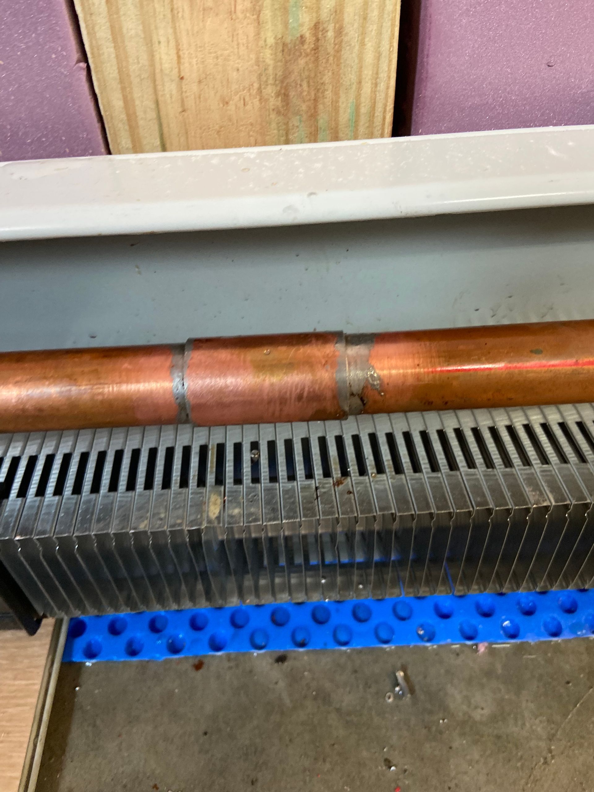 Copper pipe with a soldered joint resting on a black radiator with a blue mat.