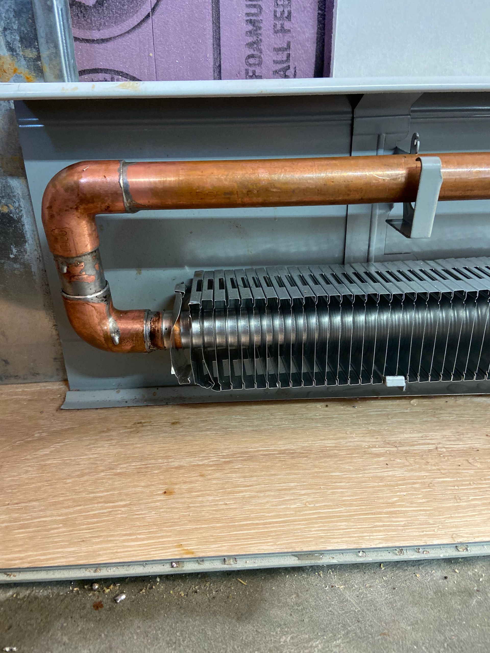Copper pipe connected to a finned baseboard heater, secured with a metal bracket in a basement setting.
