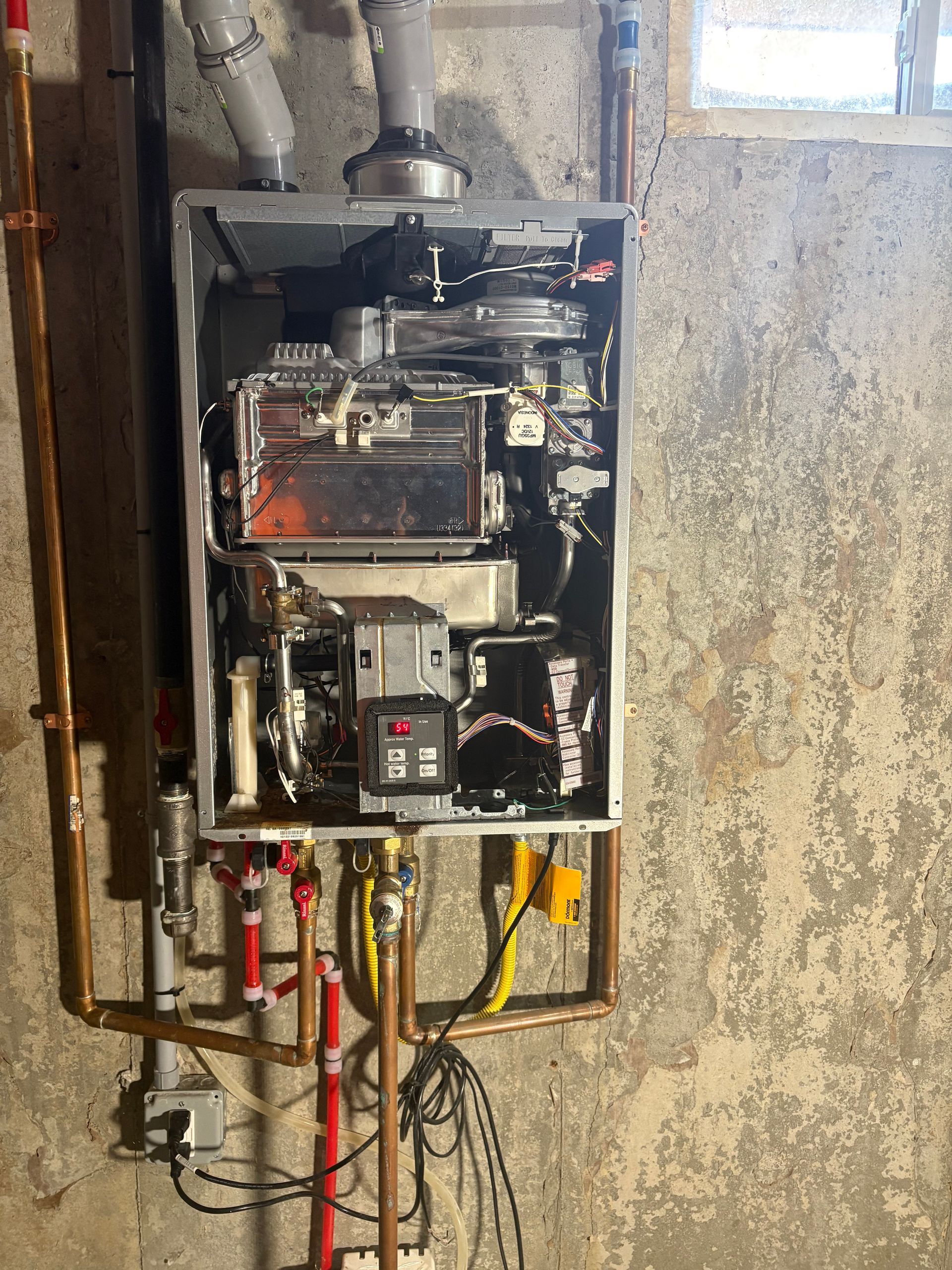 A wall-mounted boiler with copper pipes, vents, and a digital control panel, set against a concrete wall.